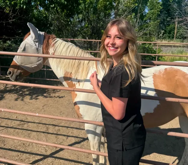 Young woman smiling with a horse at a ranch, representing community involvement.