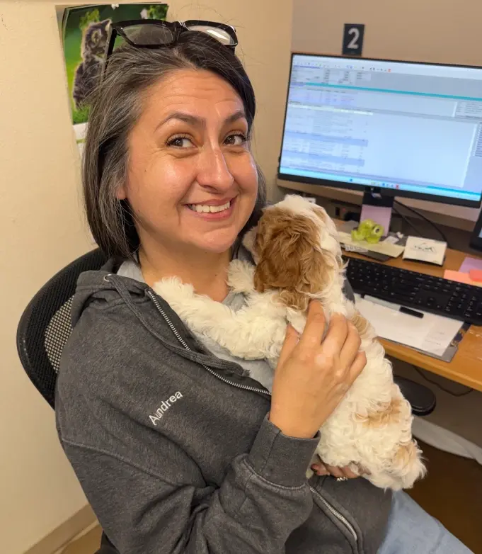 Smiling dental team member holding a small dog in an office setting.