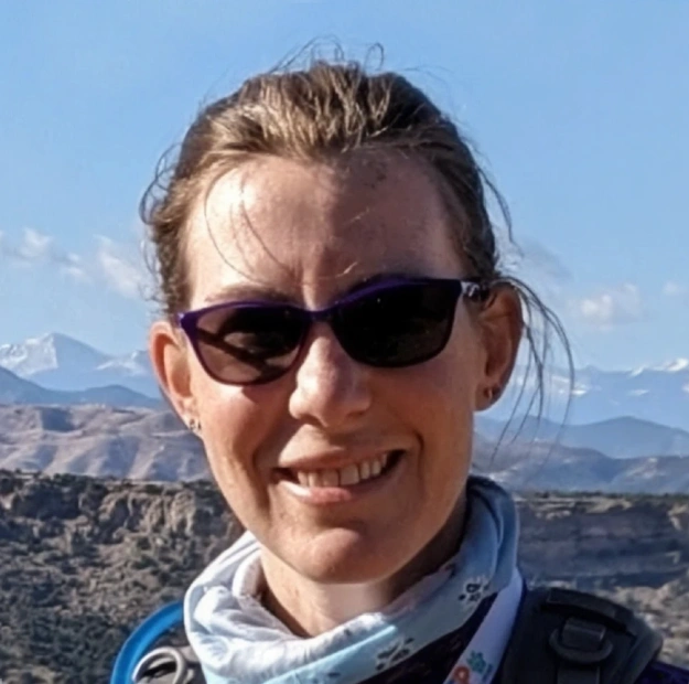 Dr. Nicodemus smiling outdoors in sunglasses with a mountain landscape in the background